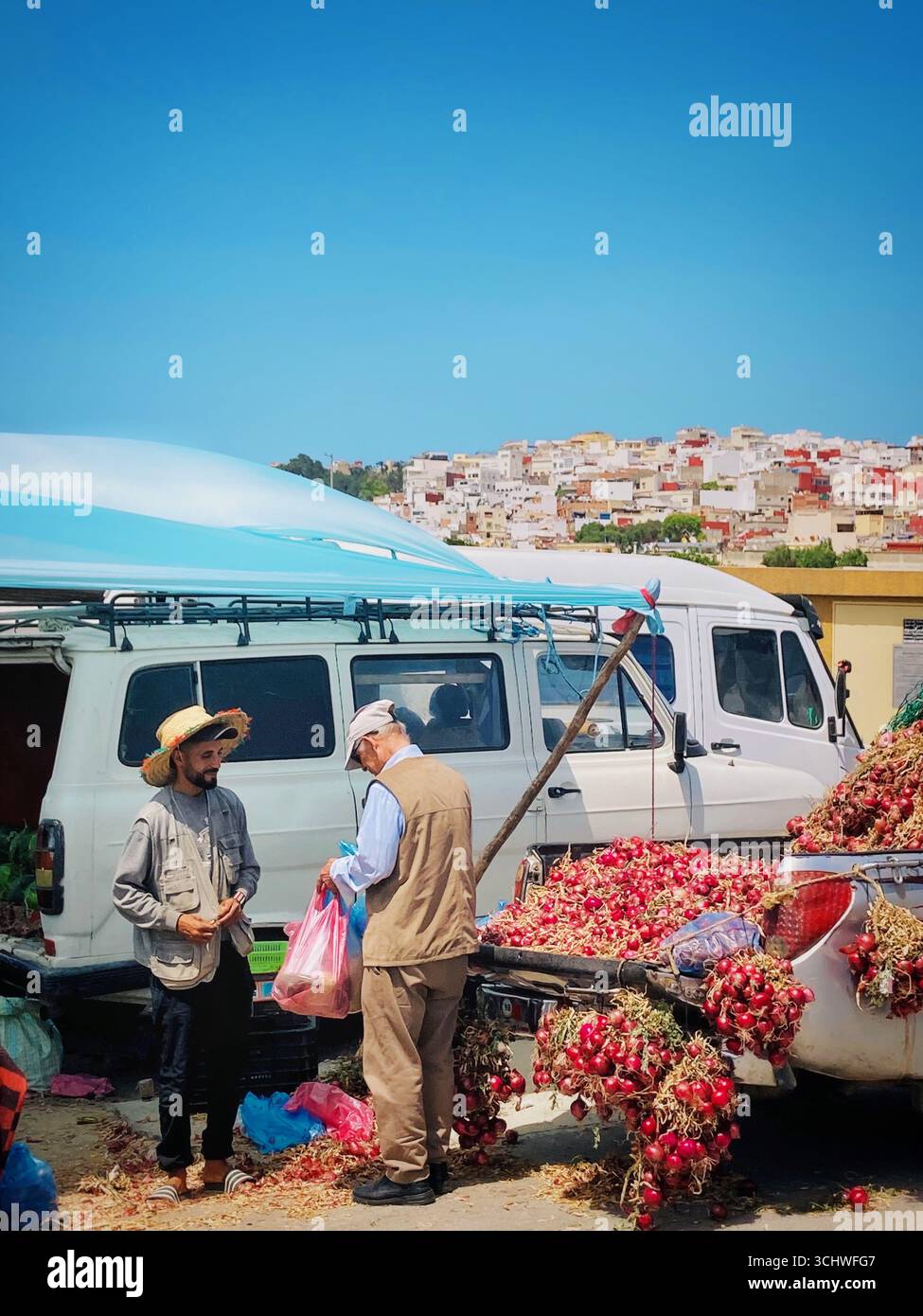I venditori locali al Dradeb Market di Tangeri si impegnano nel commercio di cipolle vicino a pick-up e bancarelle ombreggiate, Tangeri, Marocco. 6 giugno 2023. Foto Stock