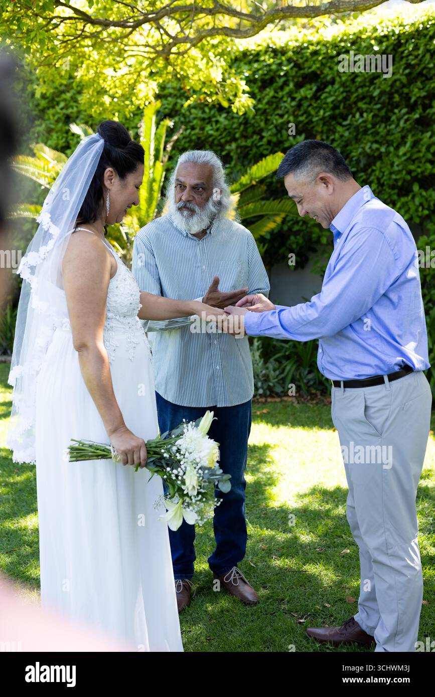 Si scambiano anelli, diverse coppie con l'officiante durante la cerimonia di nozze in giardino Foto Stock
