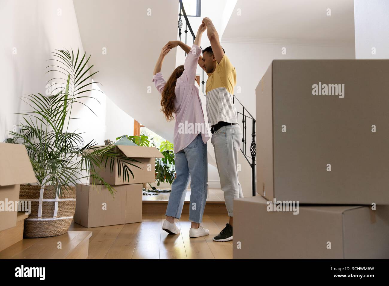 Giovani coppie diverse che ballano gioiosamente in una nuova casa circondata da scatole in movimento Foto Stock