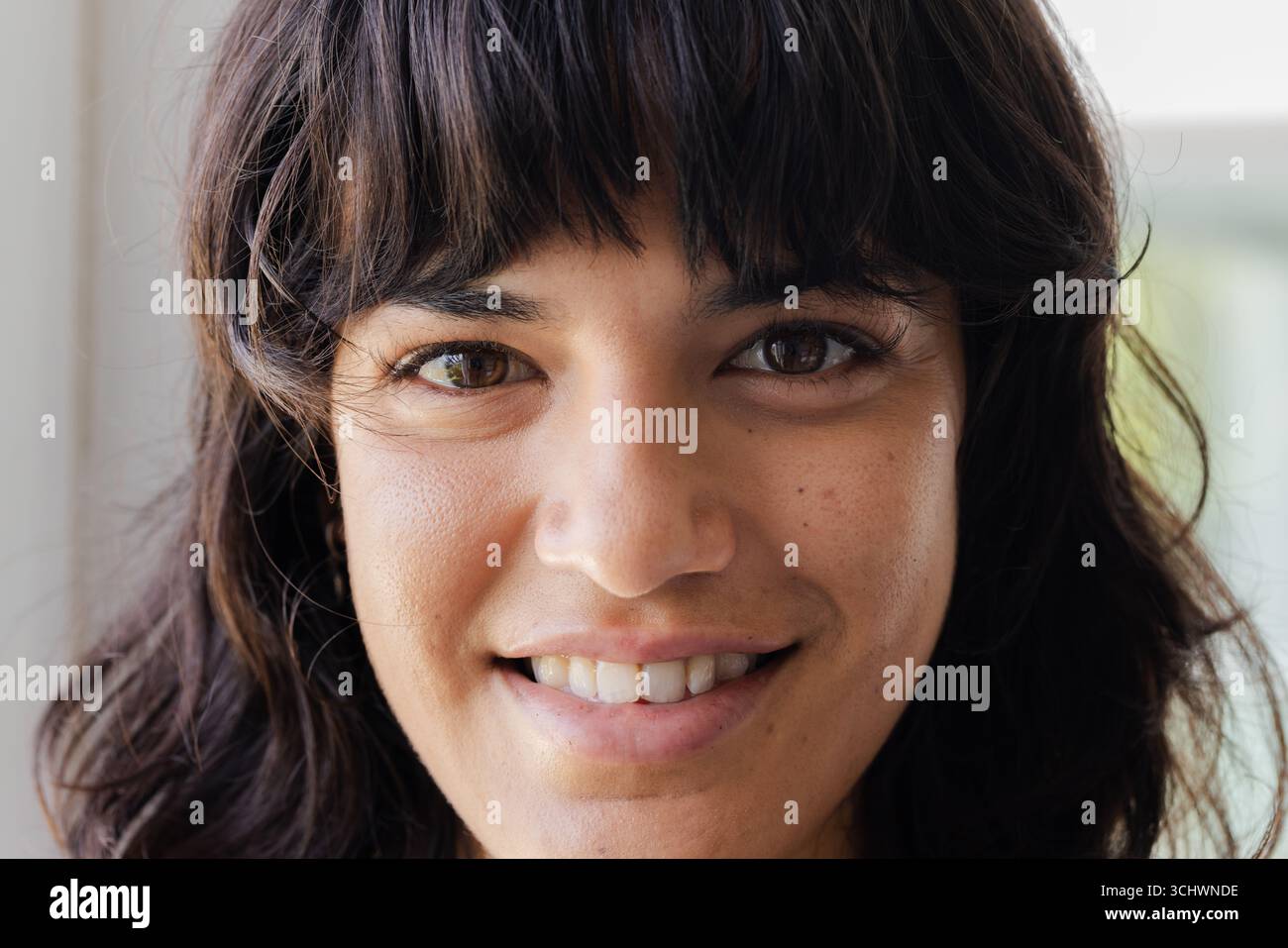 Donna sorridente con capelli scuri che guarda la fotocamera, mostrando felicità Foto Stock