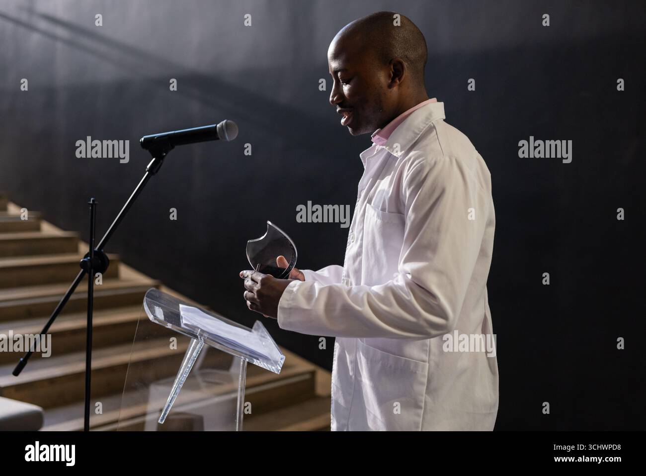 Uomo in camicia bianca che parla al podio tenendo un premio, presentando alla conferenza Foto Stock