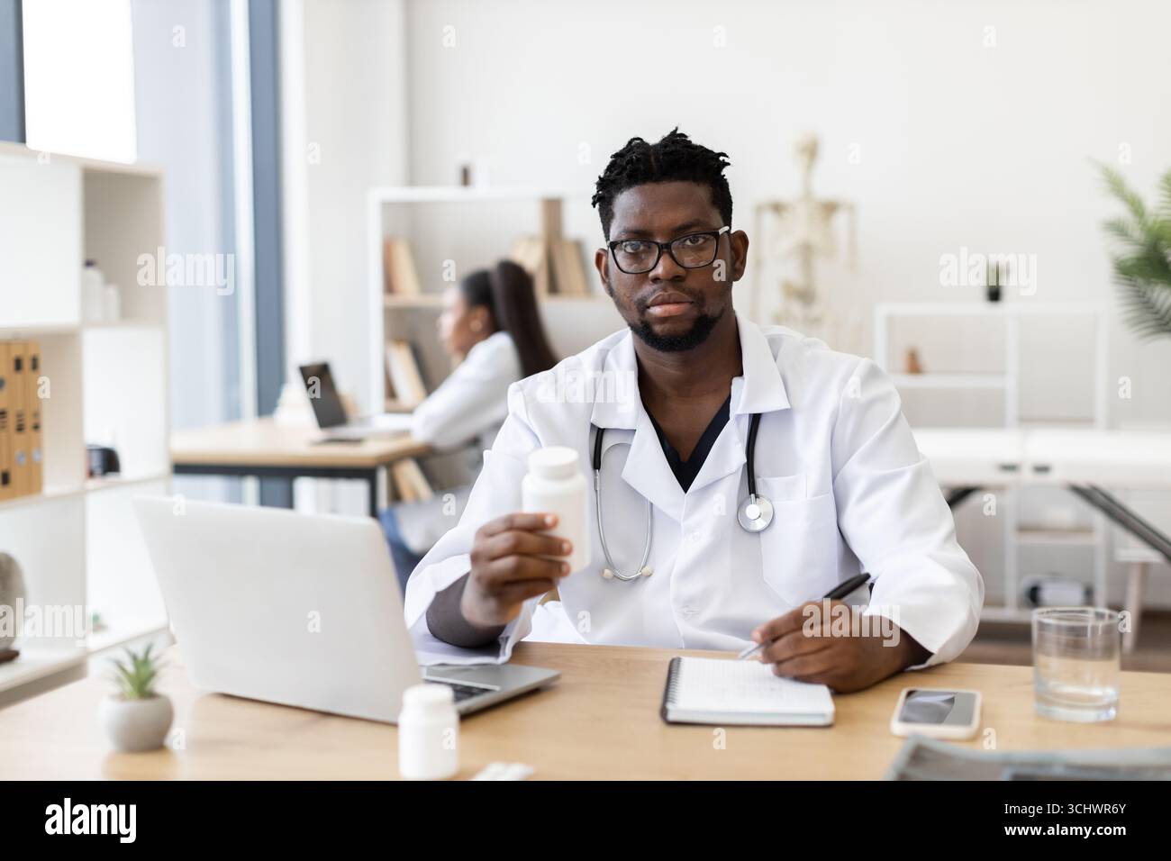 Medico di sesso maschile consulenza e scrittura prescrizioni in moderno ufficio medico Foto Stock