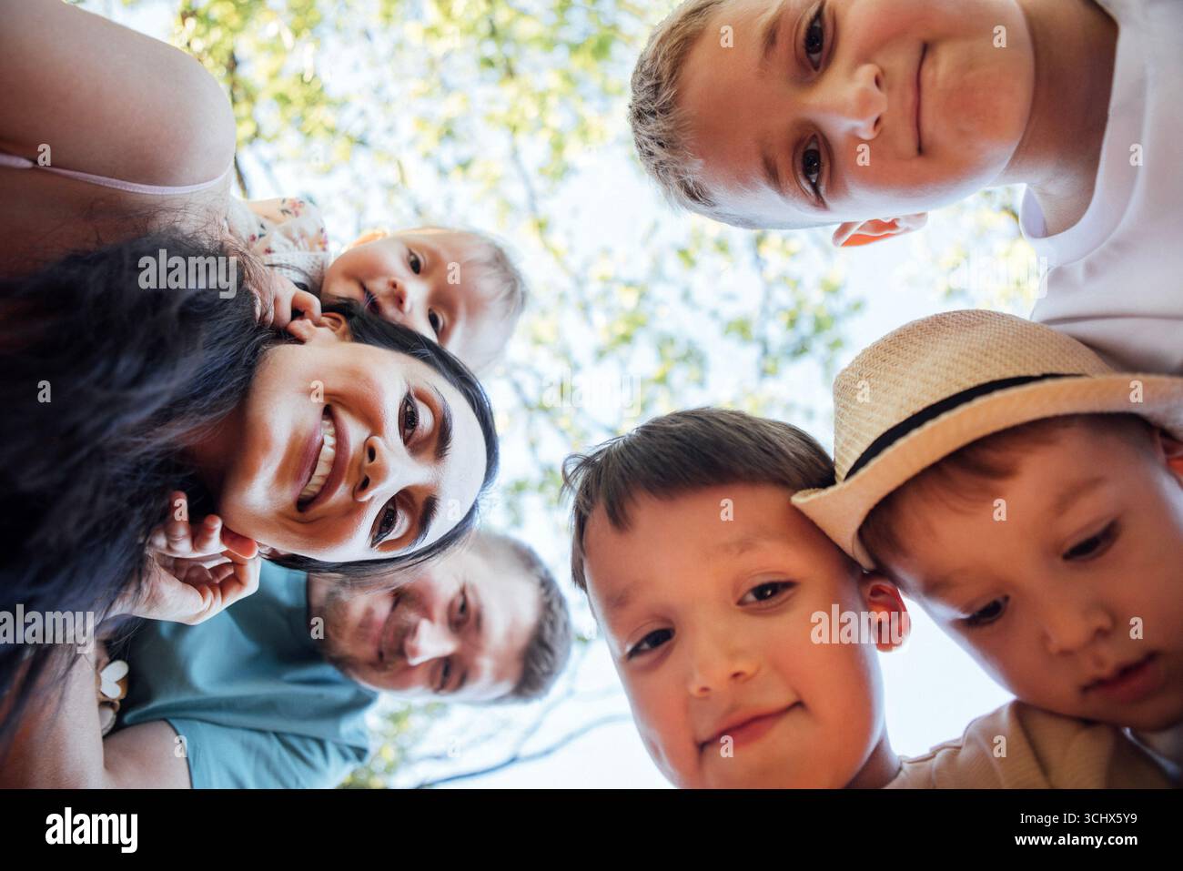 Famiglia felice di bambini e adulti che sorridono insieme da un angolo basso, circondati da una vegetazione lussureggiante, creando un'atmosfera gioiosa e giocosa nella natura Foto Stock