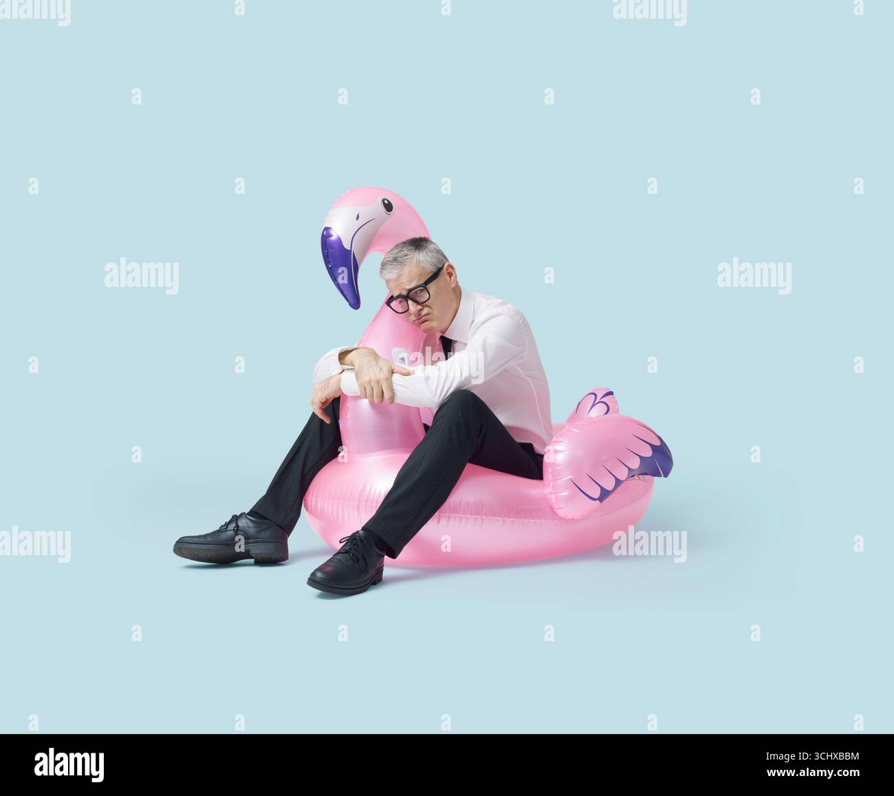 Divertente uomo d'affari depresso seduto su un giocattolo gonfiabile flamingo, l'estate è finita e deve tornare al lavoro Foto Stock
