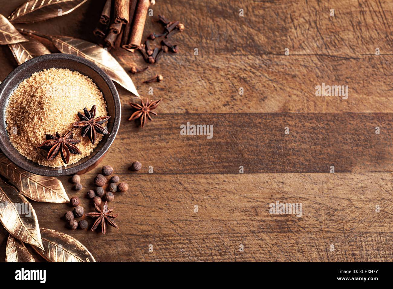 Zucchero di canna con spezie invernali e decorazioni natalizie dorate su sfondo in legno, vista dall'alto, spazio fotocopie. Concetto natalizio con stelle di anice, chiodi di garofano e Foto Stock