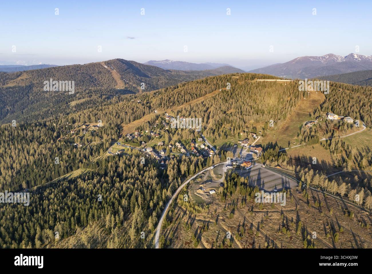 Vista aerea di una foresta estesa punteggiata da piste da sci e di un piccolo villaggio annidato tra le colline ondulate, Hochrindl, Kärnten, Austria. Foto Stock