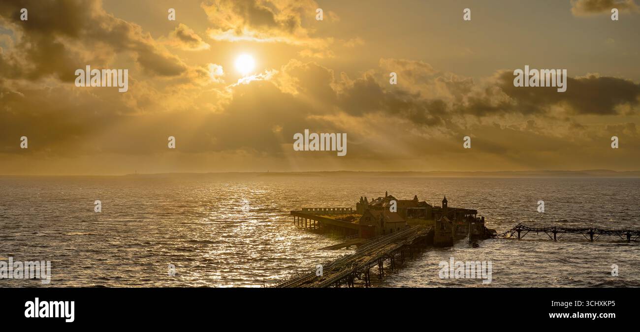 Il sole tramonta al vecchio molo di Birnbeck a Weston Super Mare, Somerset, Regno Unito, con i raggi del sole che scendono. Il molo è impostato per essere ripristinato. Foto Stock