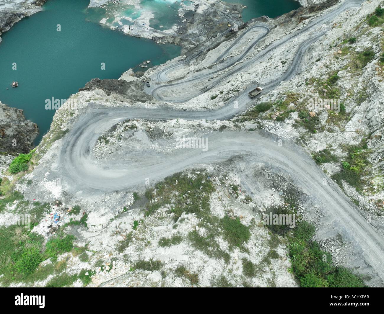 Vista aerea della cava di calcare con camion pesanti in movimento lungo strade tortuose durante le operazioni minerarie, evidenziando l'approvvigionamento di materie prime, industriali Foto Stock