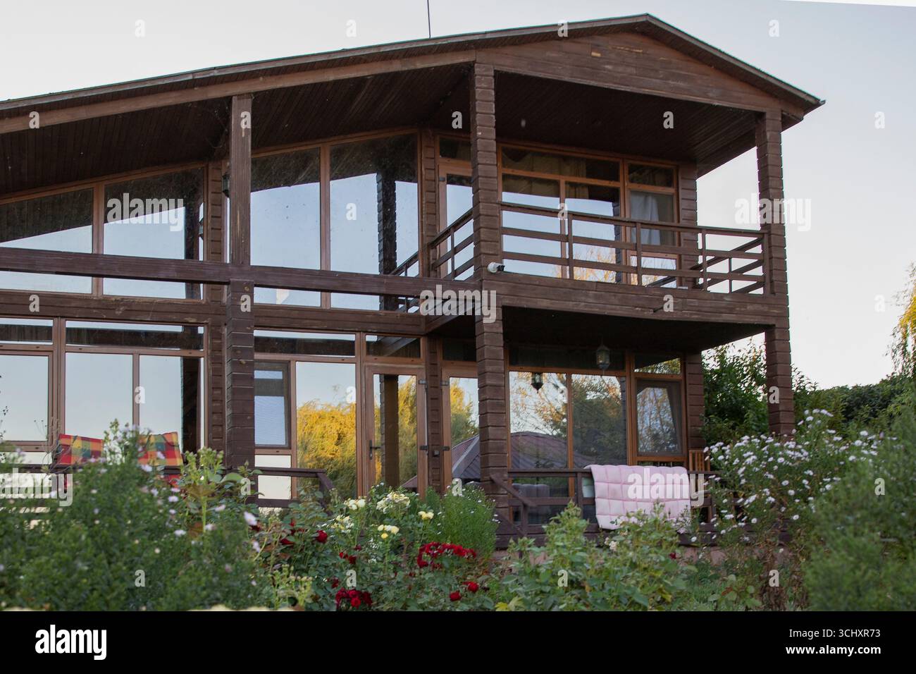 Moderna casa in legno a due piani con grandi finestre panoramiche circondata da giardino verde e piante concetto di stile di vita rurale e di sostentamento ecologico Foto Stock