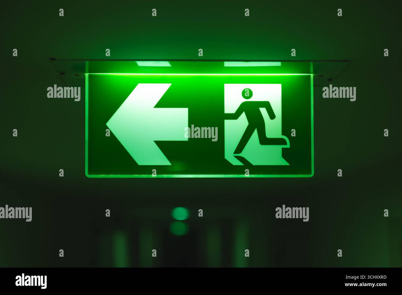 Uscita direzione freccia direzione direzione, segnale guida uscita luce verde segnale uscita di emergenza in una stanza buia installazione sul corridoio dell'edificio a soffitto corri Foto Stock