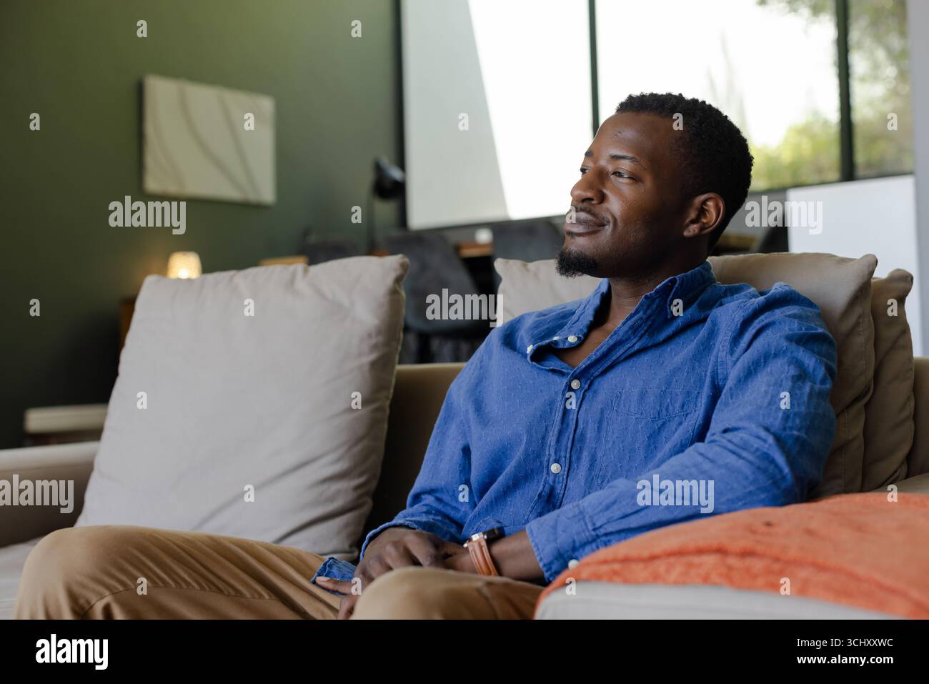 Rilassatevi a casa, uomo afroamericano seduto sul divano, che sembra contento Foto Stock