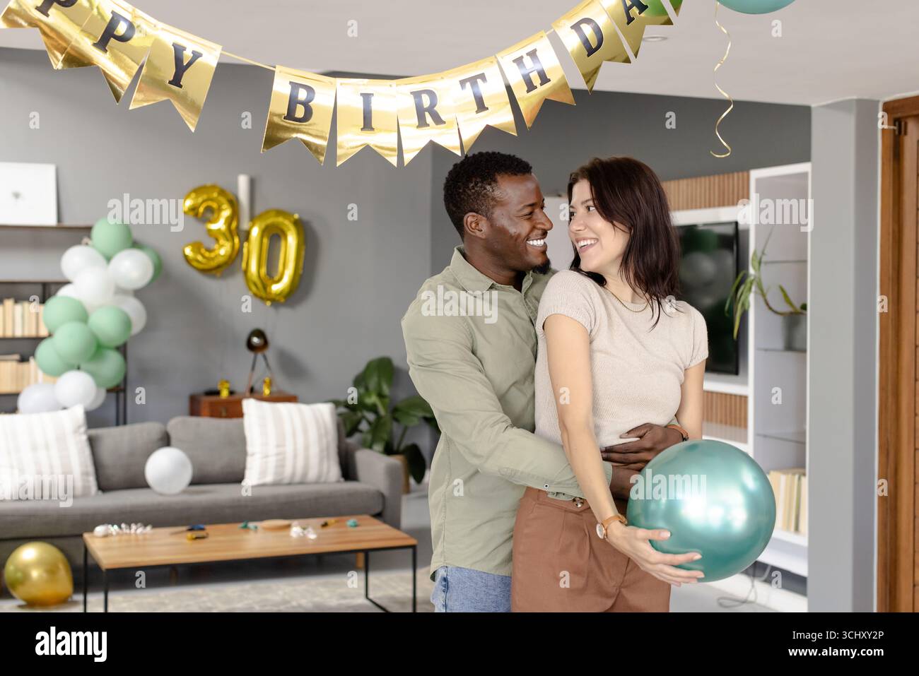 Festeggiamo il 30° compleanno con palloncini, uomo e donna afroamericani sorridenti a casa Foto Stock