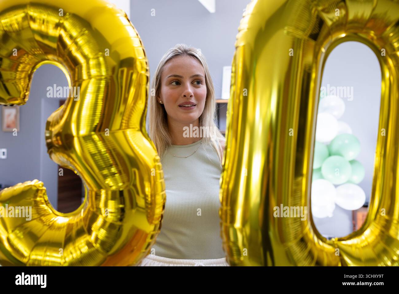 Alla festa, donna che festeggia il 30° compleanno con palloncini d'oro, sorride a casa Foto Stock