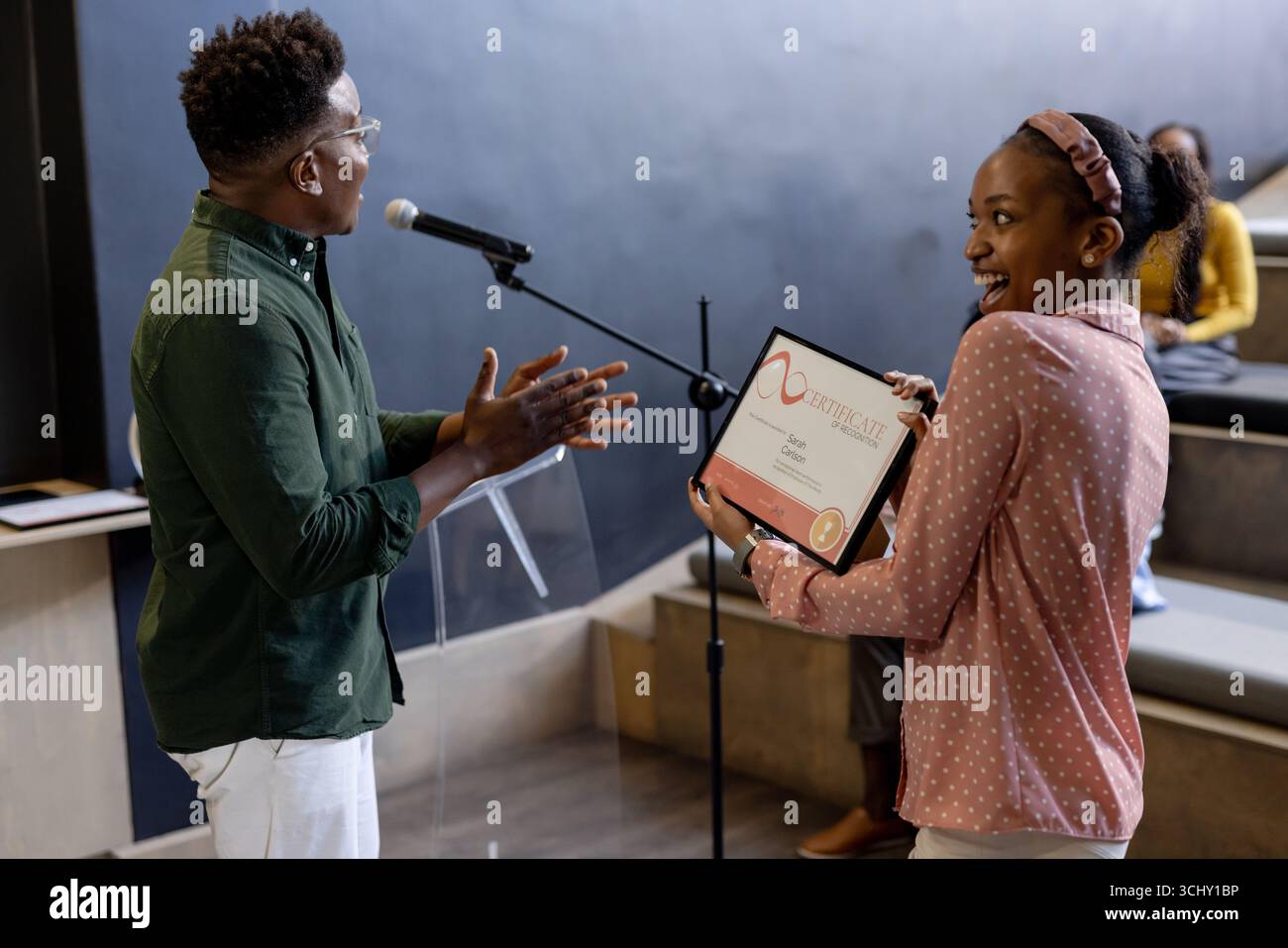 Donna che riceve il certificato sul palco, sorride mentre il pubblico applaude in ufficio Foto Stock