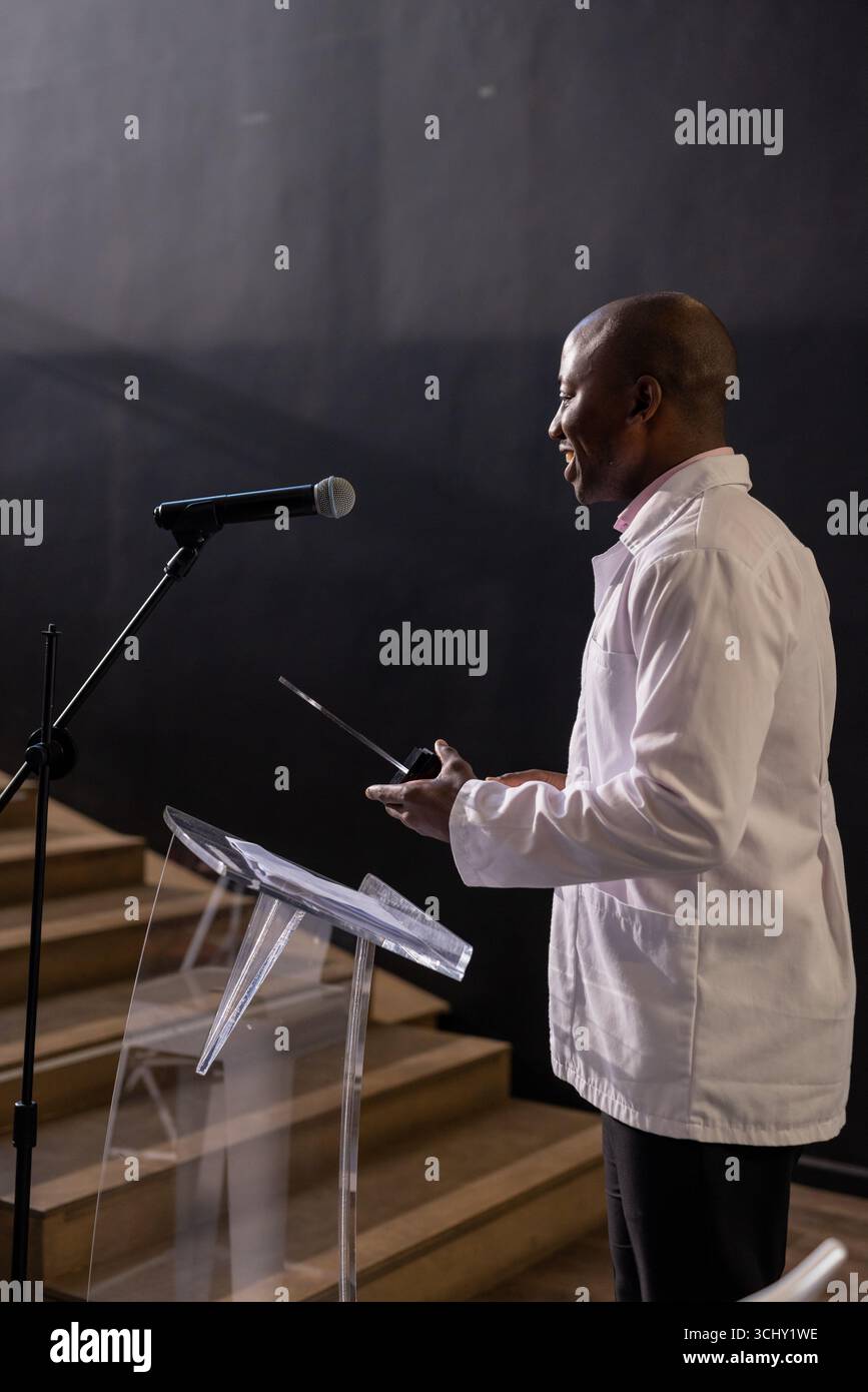 Uomo afroamericano che presenta con microfono sul podio nella sala conferenze Foto Stock