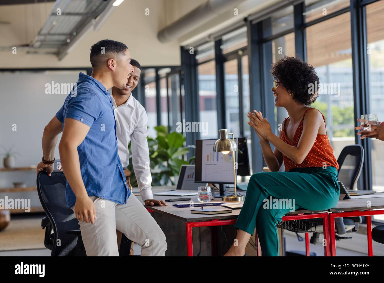 Colleghi che discutono di progetti alla scrivania dell'ufficio, condividono idee e sorridono Foto Stock