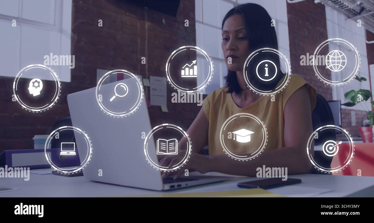 Donna matura che indossa la mostarda sulla scrivania dell'ufficio, sul laptop e sulle icone digitali sovrappongono lo spazio di copia Foto Stock