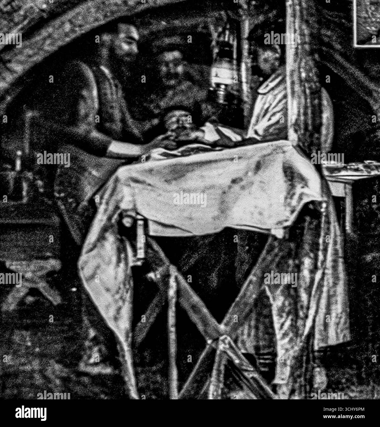 Foto in bianco e nero di l'Illustration, 1916, che mostra l'interno a volta di una cabina di vestizione in prima linea. Un medico francese tende a un soldato ferito su un tavolo, con attrezzature nelle vicinanze, tra cui secchi di soluzione protettiva per l'esposizione al gas. L'immagine evidenzia le dure realtà della chirurgia in tempo di guerra e la resilienza del personale medico che lavora in ospedali sotterranei improvvisati durante la prima guerra mondiale Foto Stock