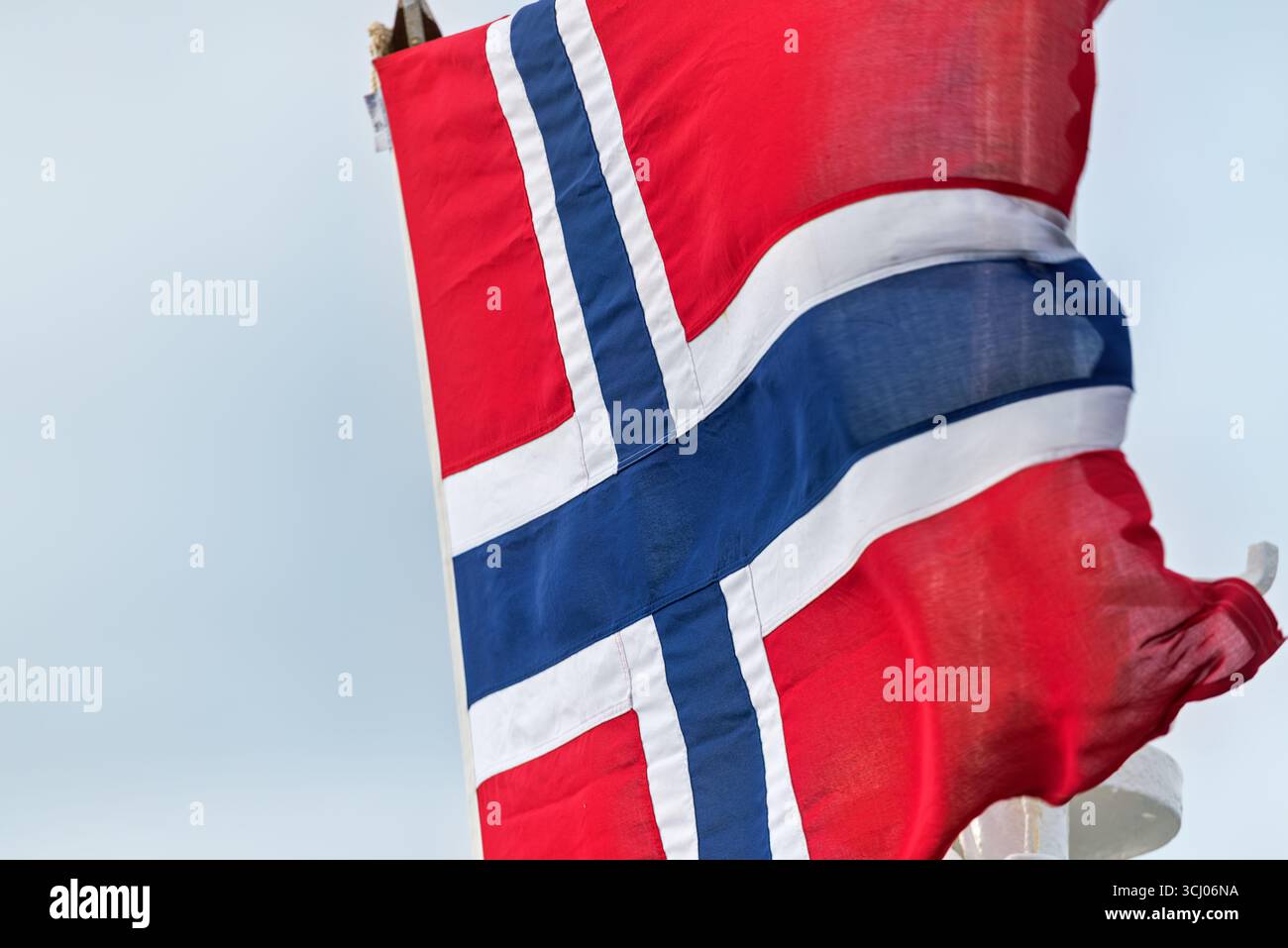 Bandiera norvegese che sventola a Longyearbyen Svalbard Norvegia | LONGYEARBYEN, Svalbard e Jan Mayen — La bandiera norvegese, una croce scandinava blu bordata di bianco su campo rosso, sventola contro un cielo artico pallido sopra Longyearbyen. Il trattato di Svalbard, firmato a Parigi il 9 febbraio 1920, ha riconosciuto la piena sovranità norvegese sull'arcipelago, formalizzata con la legge di Svalbard del 17 luglio 1925. La clausola insolita di accesso aperto del trattato, che concede uguali diritti di residenza e lavoro ai cittadini di tutti gli Stati firmatari, ha dato a Longyearbyen una popolazione proveniente da circa 40 nazionalità. Foto Stock