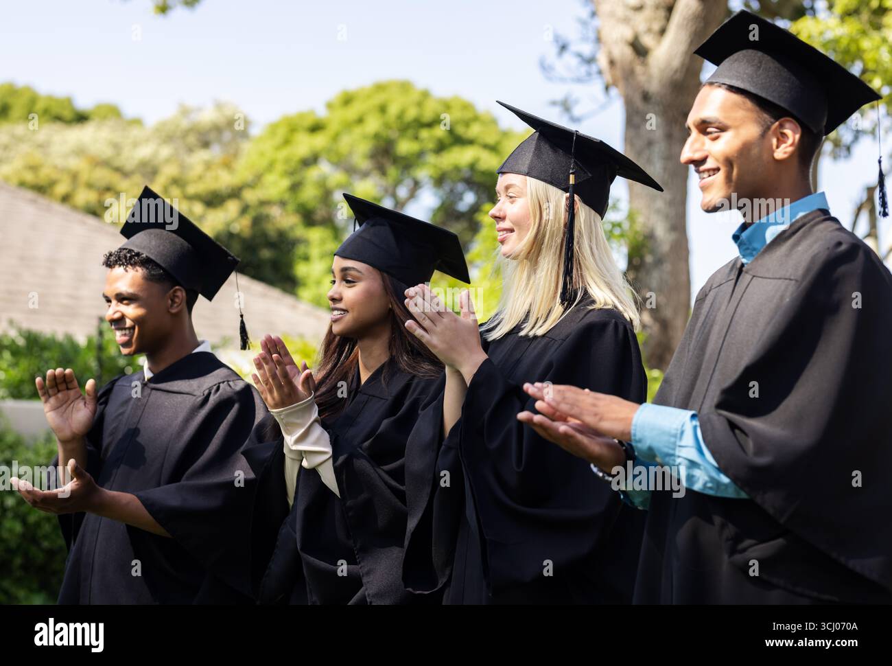 Diversi laureati in cappelli e abiti che battono in giardino, celebrando il loro successo Foto Stock