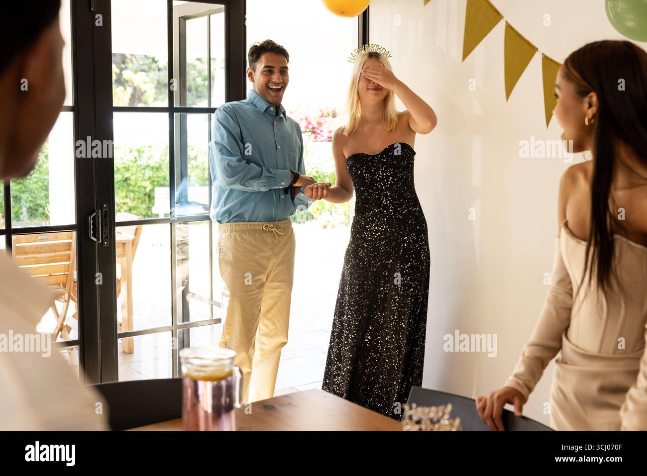 Amici eterogenei che sorprendono la donna con festeggiamenti di compleanno a casa, condividendo risate gioiose Foto Stock