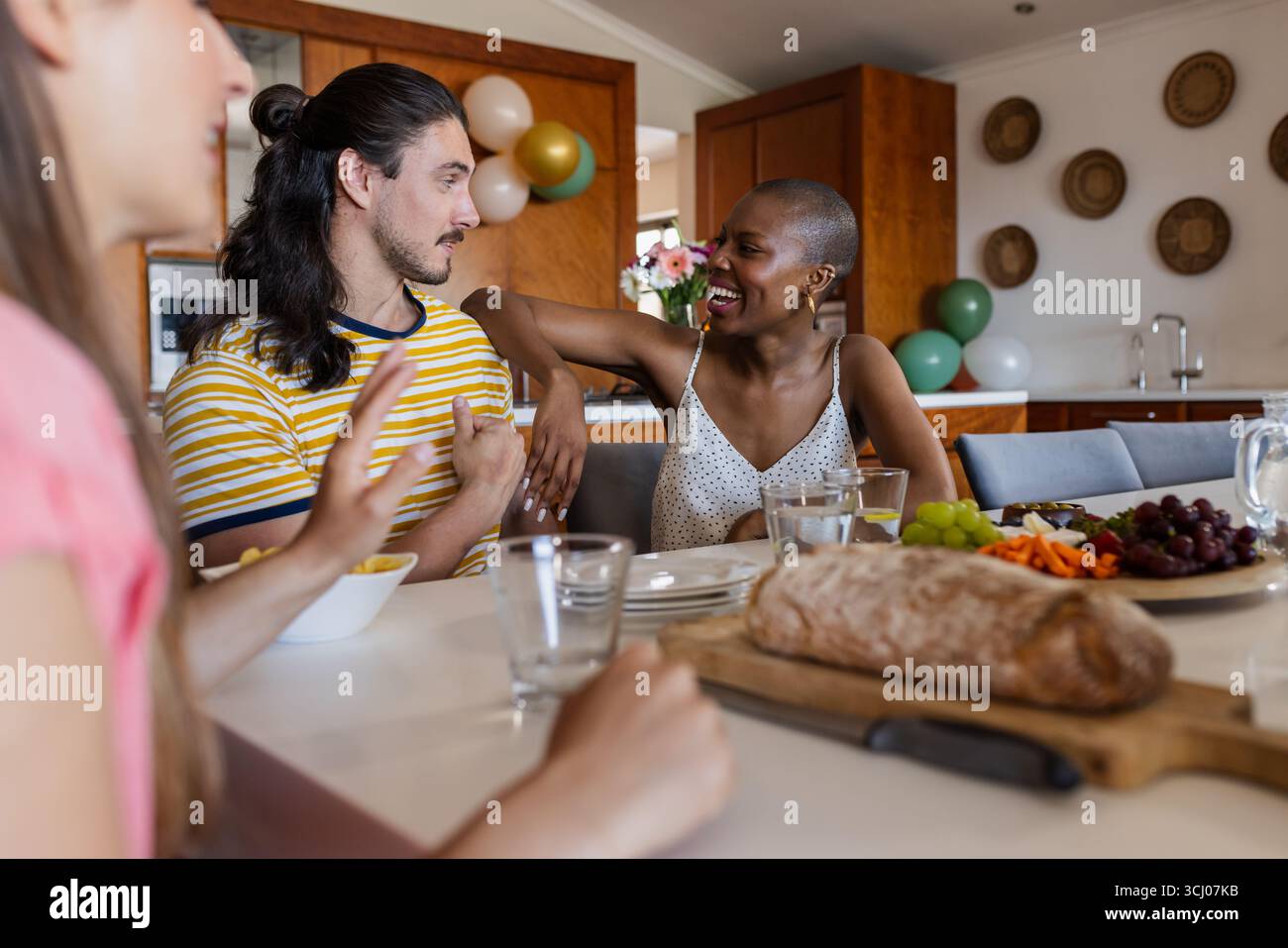 Amici che si godono la conversazione e gli spuntini a casa, condividendo risate e storie Foto Stock