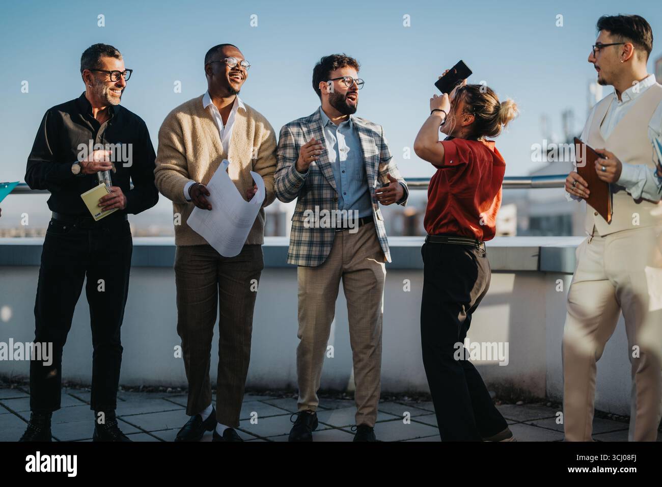 Team di lavoro diversificato che festeggiano sul tetto al tramonto Foto Stock