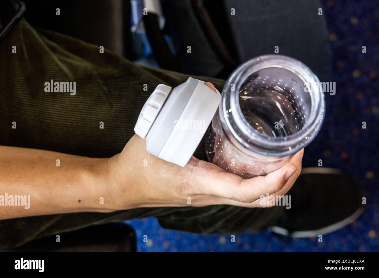 Mano che tiene il bicchierino trasparente vuoto durante il viaggio per riempire l'acqua nell'aeroplano per l'idratazione durante il volo Foto Stock