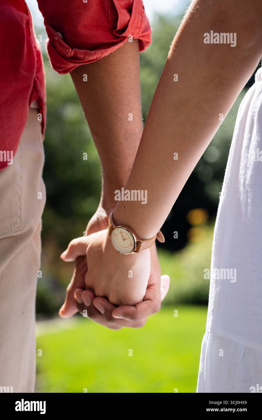 Diverse coppie che si tengono per mano in giardino, indossano abiti informali e si godono una giornata di sole insieme Foto Stock