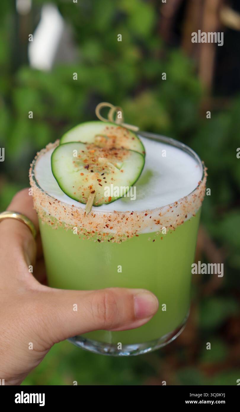cocktail verde tenuto in mano su un morbido sfondo verde naturale. Il bicchiere corto ha un bordo unico e speziato, Foto Stock