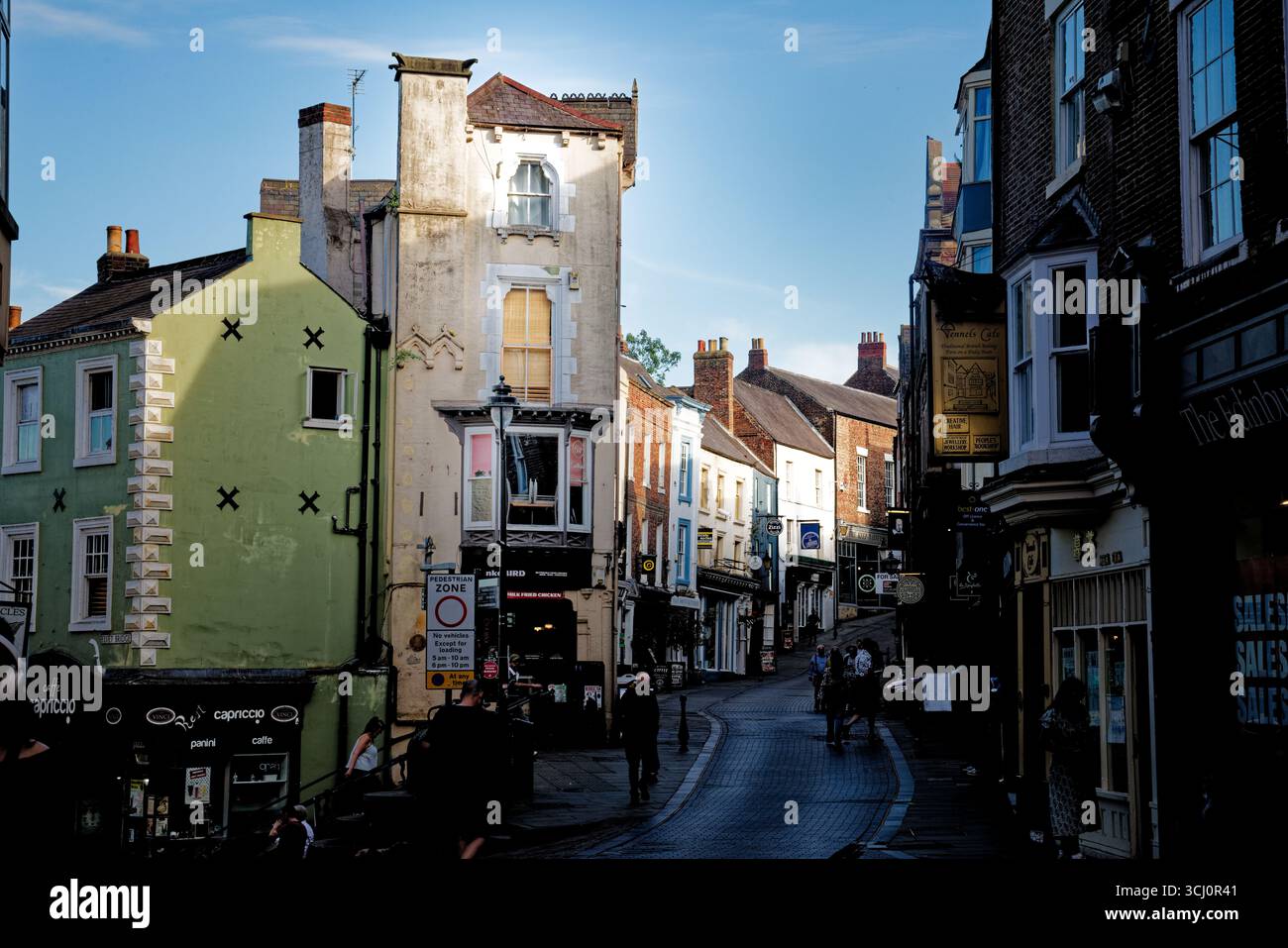 Le persone passeggiano mentre le ombre serali si insinuano lungo Sadler Street nel centro della città di Durham, in Inghilterra. Foto Stock