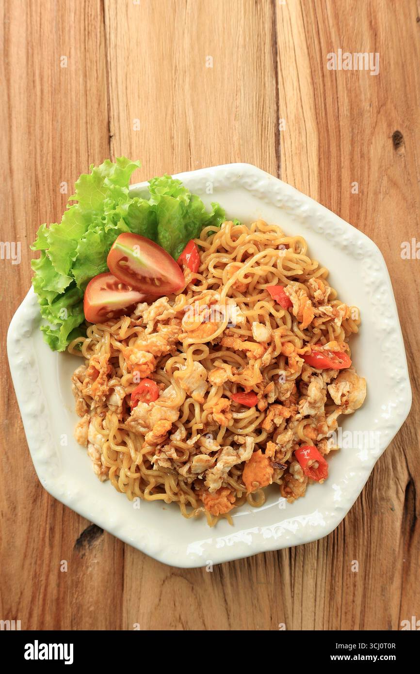 Spaghetti fritti speziati Indomie Goreng Telur, vista dall'alto su un tavolo in legno Foto Stock