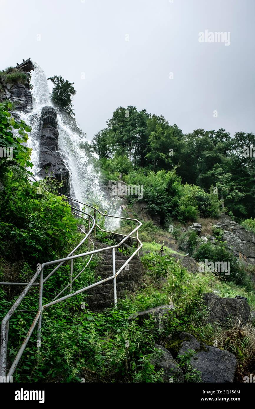 Potente cascata che scorre lungo le scogliere rocciose accanto a scale rustiche in pietra, circondata da fitte foreste, perfetta per l'avventura e il viaggio Foto Stock Potente cascata che scorre lungo le scogliere rocciose accanto a scale rustiche in pietra, circondata da fitte foreste, perfetta per l'avventura e il viaggio Foto Stock