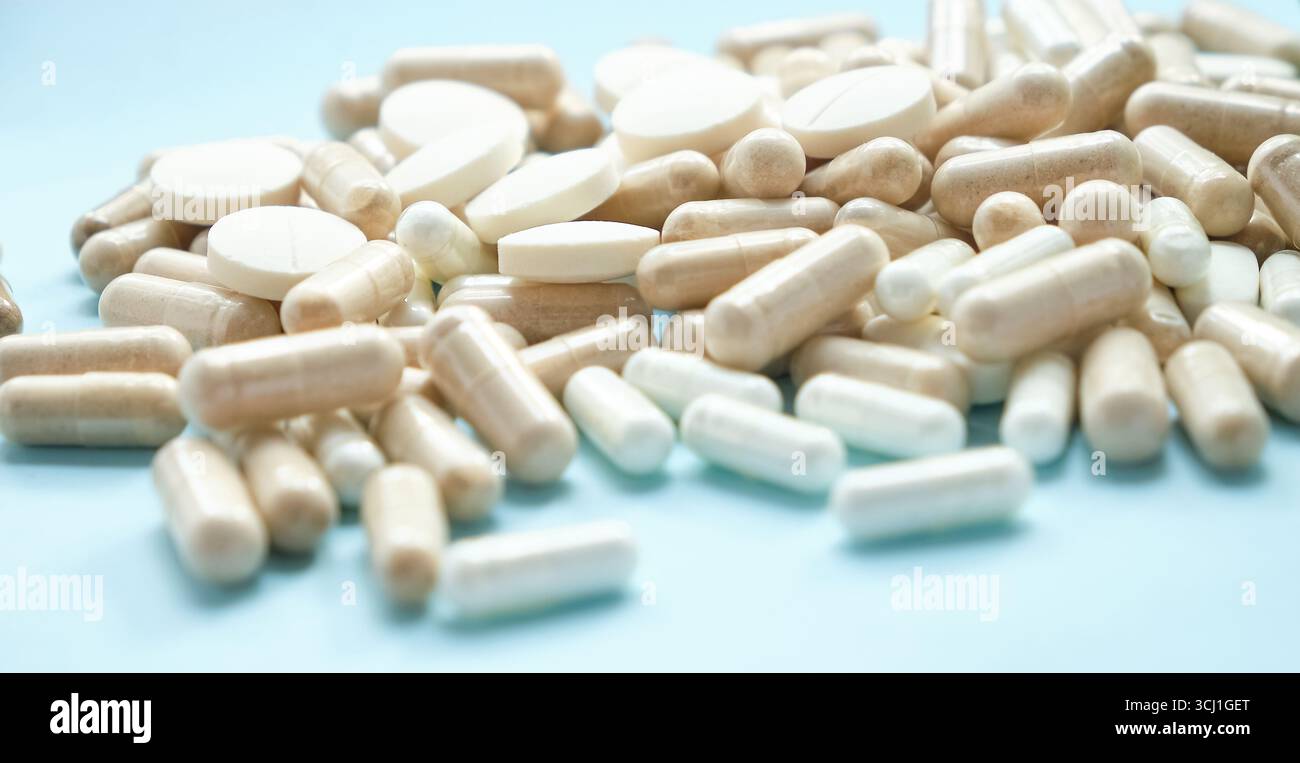 Vista ravvicinata di compresse e capsule bianche miste sparse su una superficie blu. Sfocatura e messa a fuoco selettiva Foto Stock