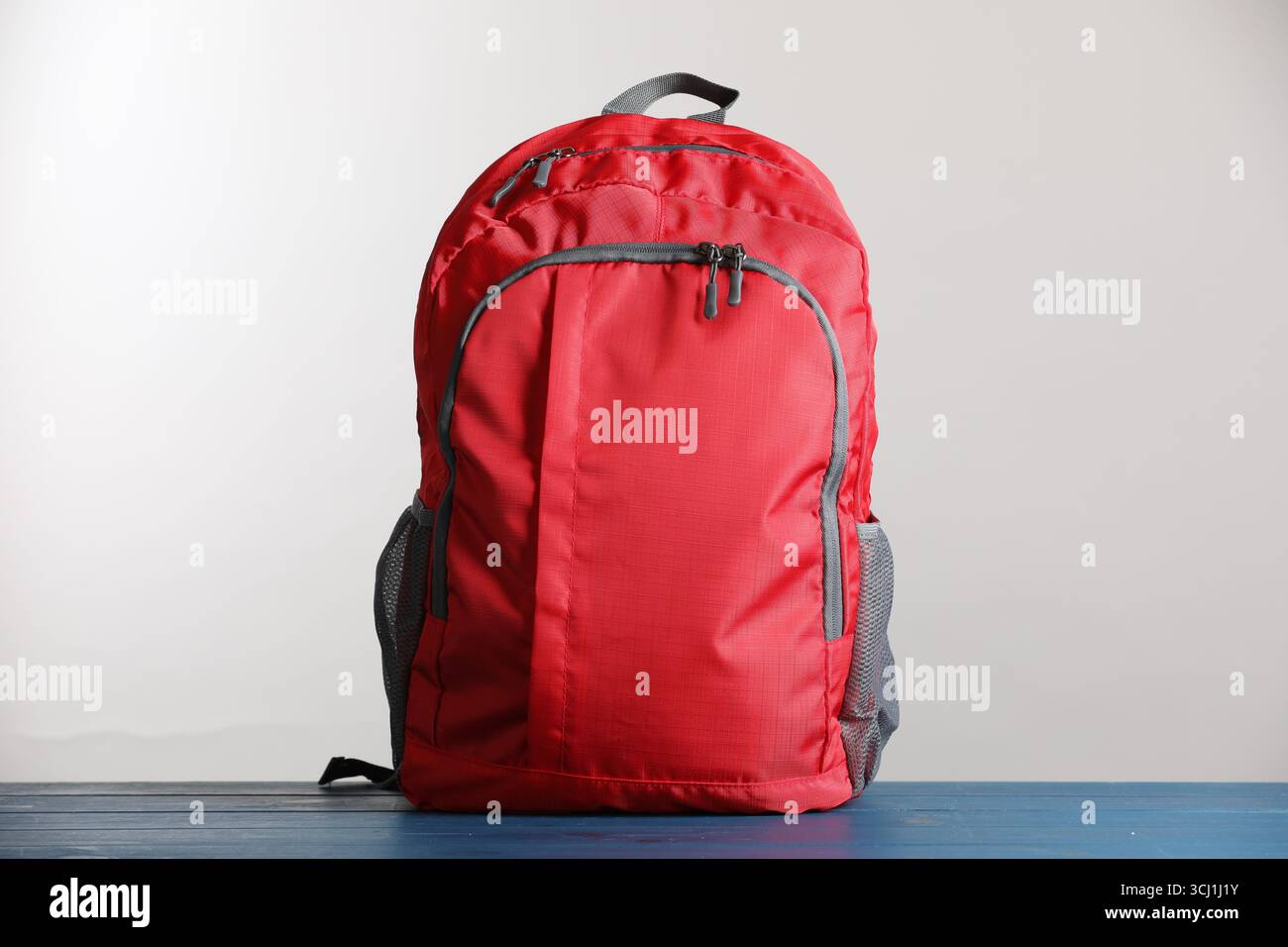 Zaino scolastico rosso su tavolo in legno blu su sfondo grigio chiaro Foto Stock