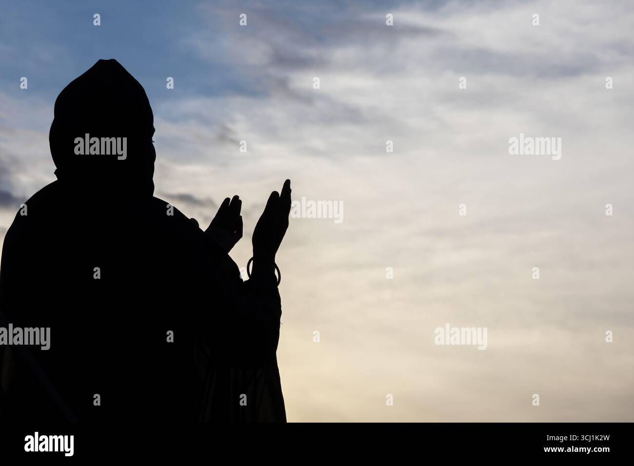 Silhouette di una donna musulmana bengalese in un abaya e un khimar che prega con le mani in alto al tramonto. Religione, fede e spiritualità. Foto Stock