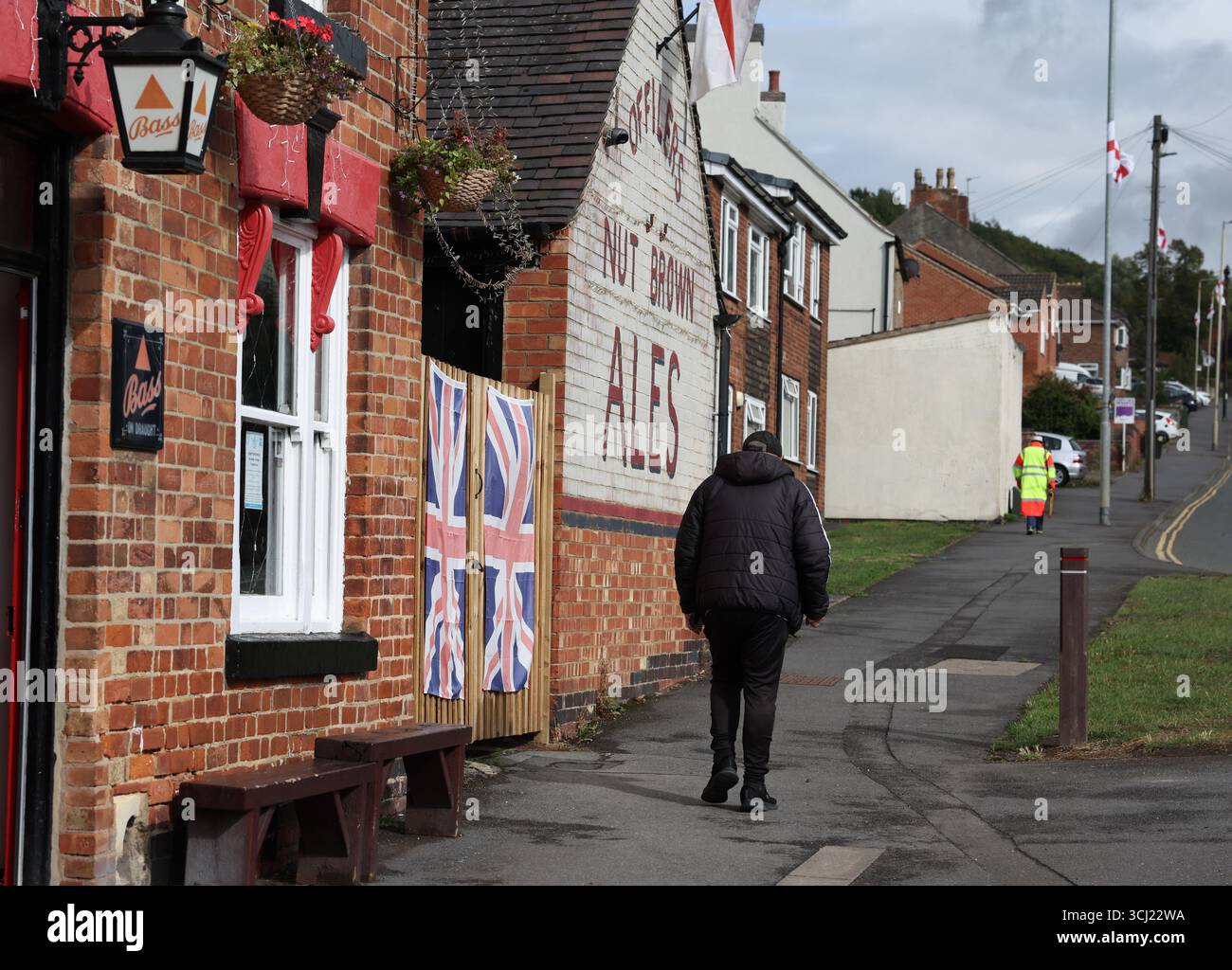 Whitwick, Leicestershire, Regno Unito. 4 settembre 2025. Un uomo cammina oltre le bandiere dell'Unione appese a un pub a causa della campagna politica ÒRaise del ColoursÓ. I sostenitori della campagna affermano che questo è allo scopo di promuovere il patriottismo e che è non di parte, anche se è stato sostenuto da diverse figure e organizzazioni associate all'estrema destra. Accreditare Darren Staples/Alamy Live News. Foto Stock