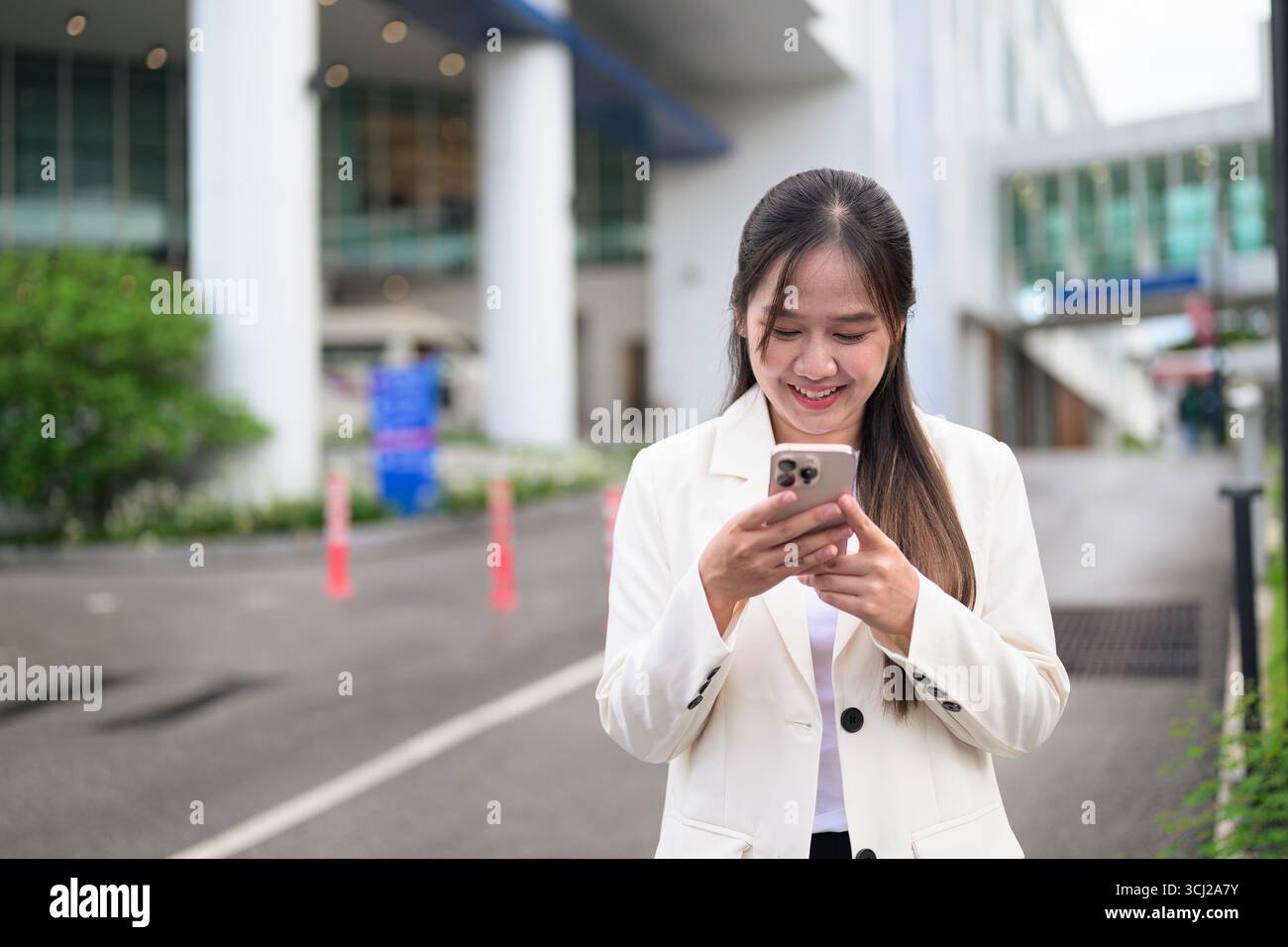 Ritratto di una donna d'affari del sud-est asiatico all'aperto nella strada della città durante il giorno, indossando abiti da lavoro e con un aspetto sicuro mentre si utilizza il telefono cellulare Foto Stock