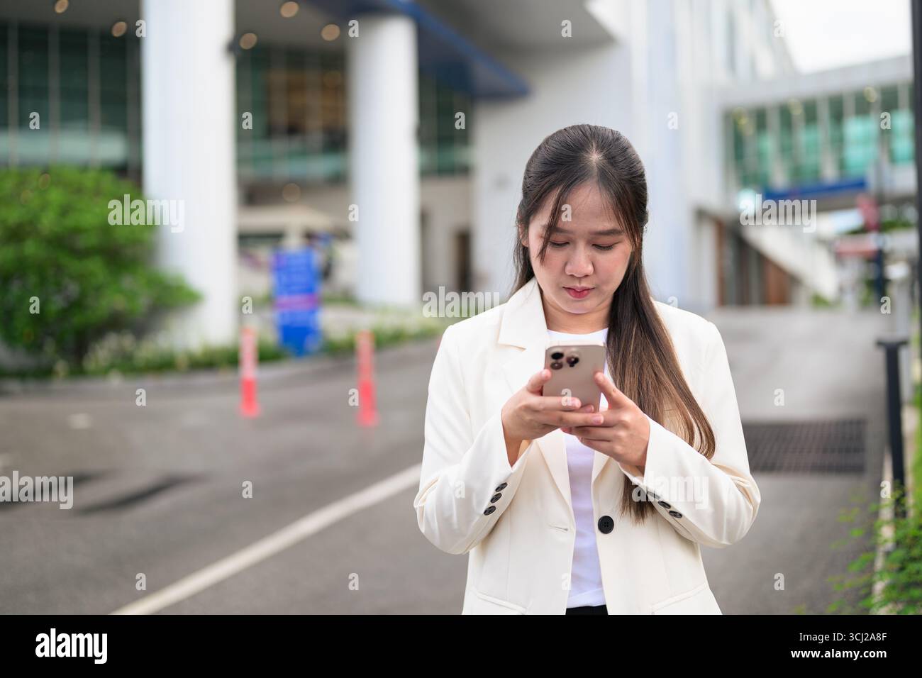 Ritratto di una donna d'affari del sud-est asiatico all'aperto nella strada della città durante il giorno, indossando abiti da lavoro e con un aspetto sicuro mentre si utilizza il telefono cellulare Foto Stock
