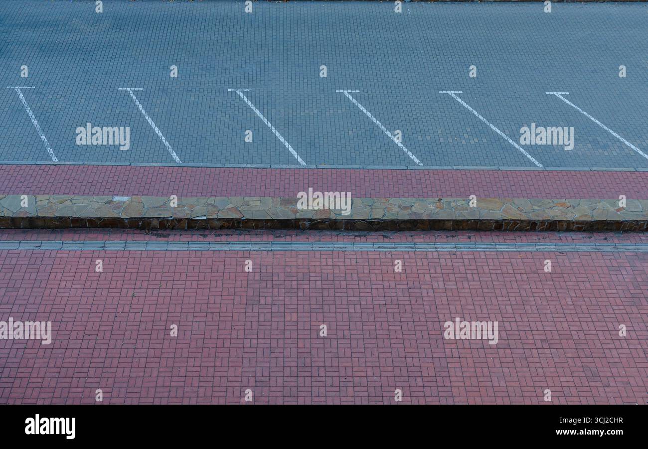 Vista dall'alto di un parcheggio vuoto con segnaletica bianca, bordo in pietra e pavimentazione in mattoni rossi. Foto Stock