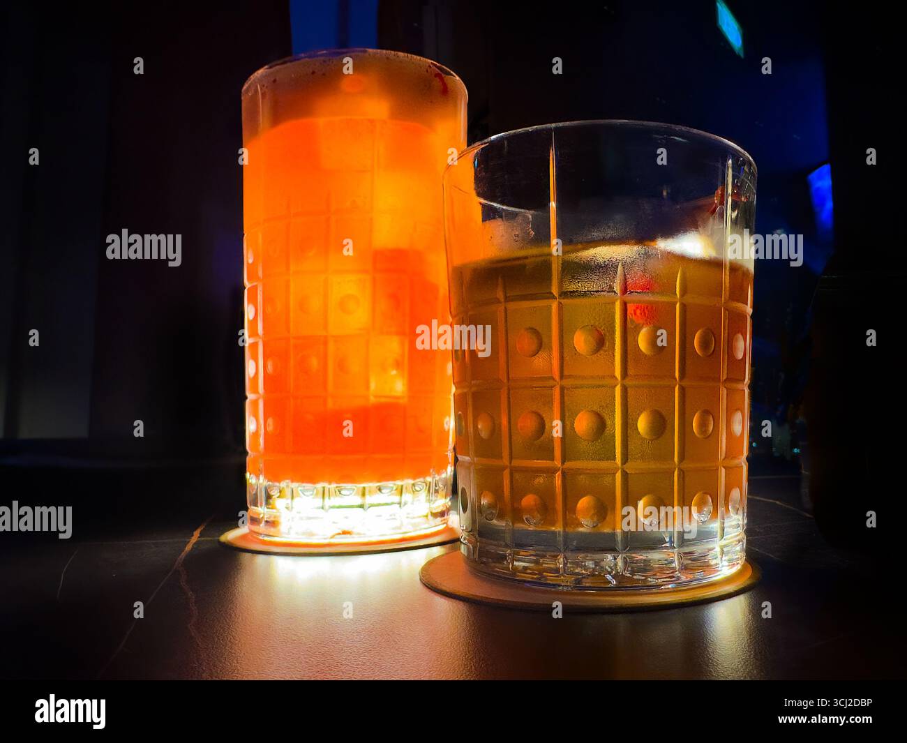 Primo piano di 2 cocktail Singapore Sling & Old Fashioned in bicchieri a motivi, tavolo illuminato fiocamente, atmosfera del Singapore Atico Lounge & bar ION Orchard Foto Stock