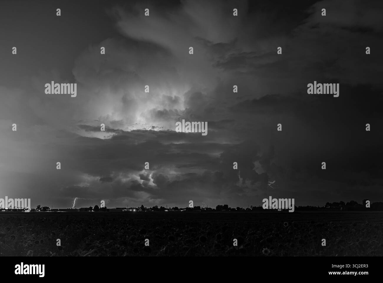 Cielo notturno tempestoso bianco e nero con fulmini lontani sull'orizzonte rurale Foto Stock