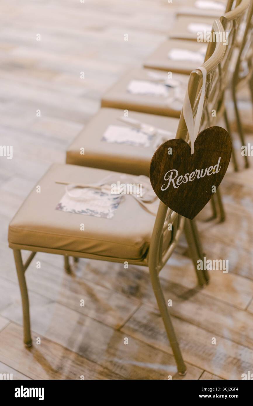 Sedie per matrimoni adornate da insegne riservate sono pronte per gli ospiti in uno spazio per eventi splendidamente organizzato. Foto Stock