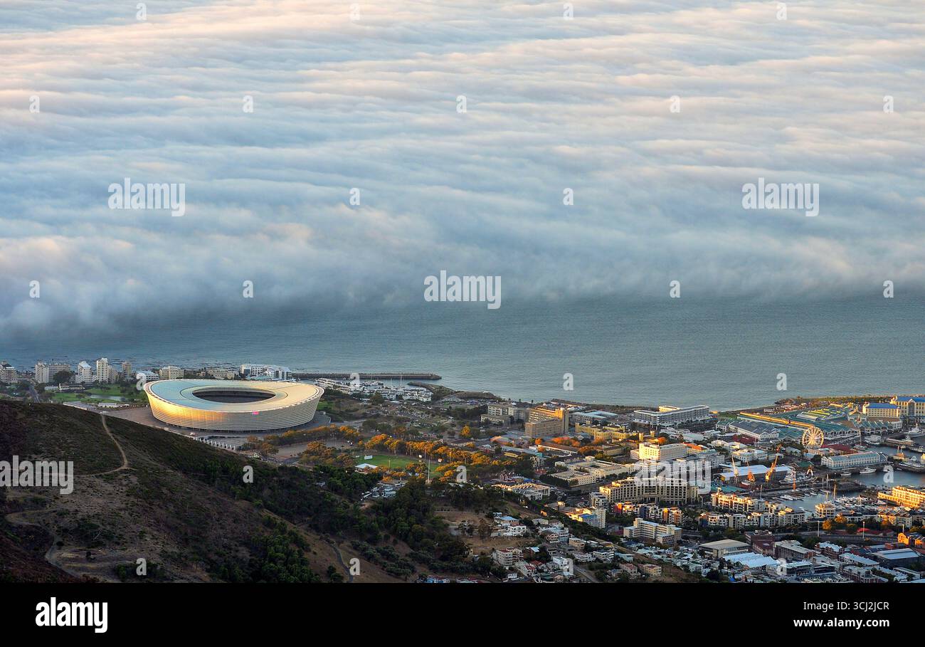 Una vista aerea di città del Capo, Sud Africa, con la città, il porto e lo stadio visibili sotto. Dall'Oceano Atlantico arriva un mare spettacolare di nuvole Foto Stock