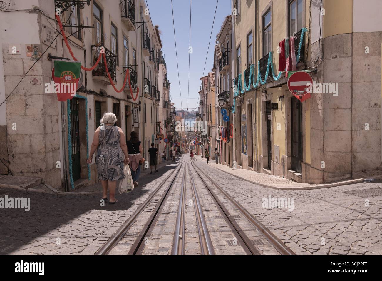 Una foto grandangolare e ad angolo basso di una strada ripida di Lisbona, che mostra le iconiche piste del tram, i classici ciottoli e un mix di architettura storica Foto Stock