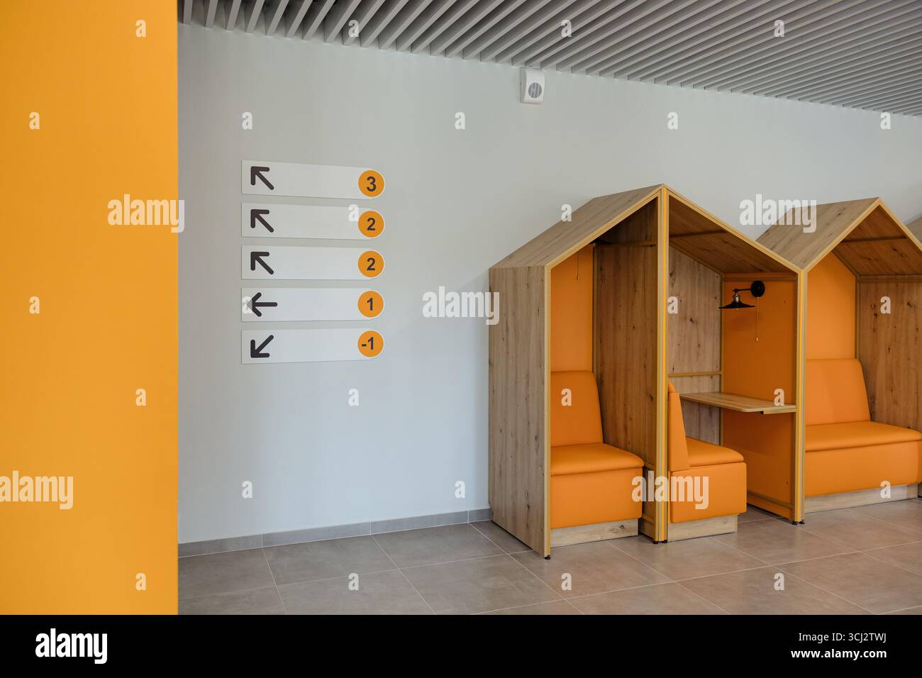 I posti a sedere arancioni luminosi sono abbinati a cartelli direzionali in un ambiente contemporaneo, creando un'atmosfera invitante per i visitatori. Foto Stock