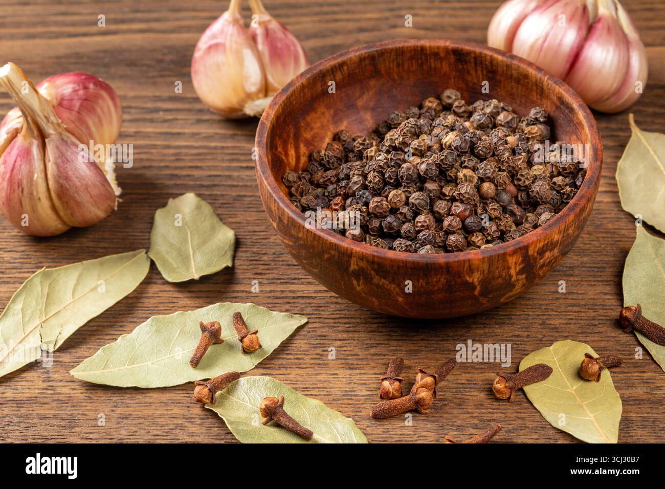 Questa foto accattivante mostra le spezie essenziali della cucina - foglia di alloro, aglio, pepe e chiodi di garofano - elegantemente disposte su un tavolo da cucina in legno, ideale Foto Stock