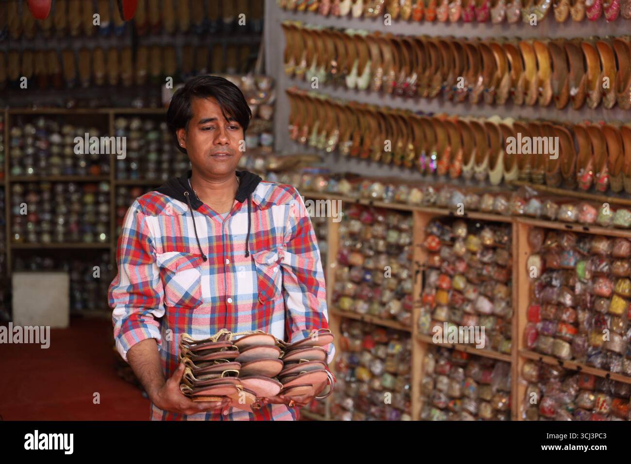 Un negoziante trasporta le tradizionali scarpe indiane dall'interno del negozio per essere esposto al Dilli Haat di Delhi, India. Foto Stock