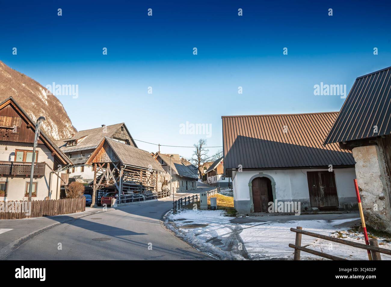Vicolo tranquillo a Stara Fuzina, Slovenia, si snoda tra fienili di legno, fienili di pietra e cottage innevati, con i loro ripidi tetti che catturano alpini di fine giornata Foto Stock