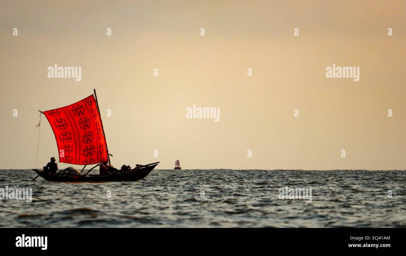 Una tradizionale barca da pesca in legno con una vivace vela rossa che attraversa la Baia del Bengala, Bangladesh. Il fascino intramontabile della vita costiera. Foto Stock